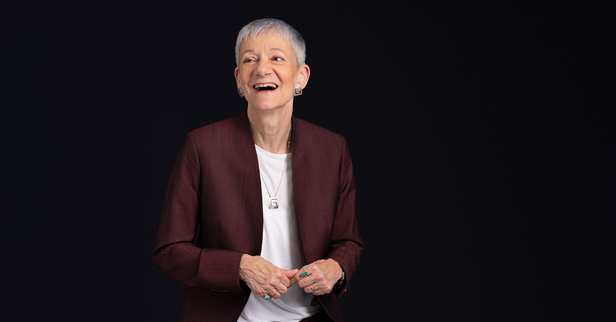 Headshot photograph of Jackie Leach Scully smiling and standing in front of a black background